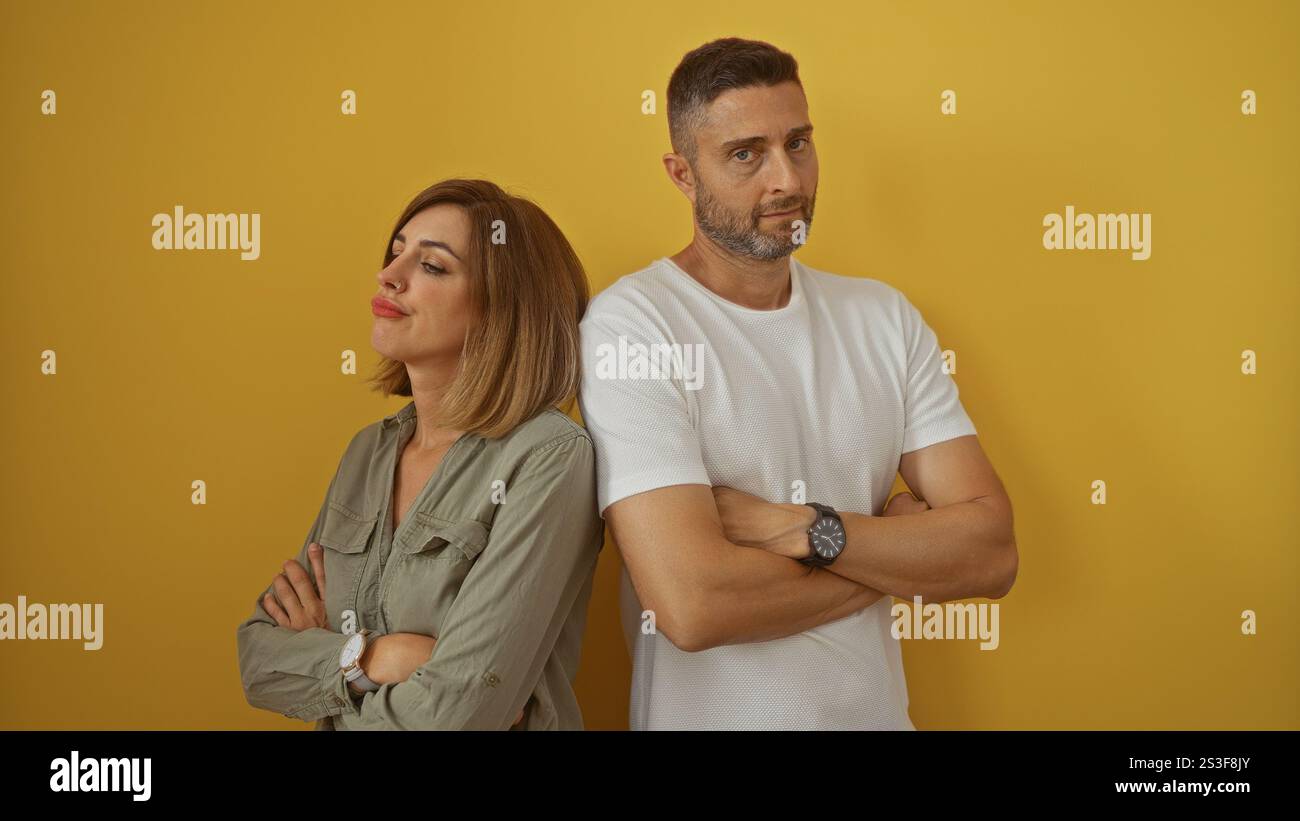 Frau und Mann stehen mit gekreuzten Armen gegen eine gelbe Wand und drücken Frustration und Distanz in ihrer Beziehung aus. Stockfoto