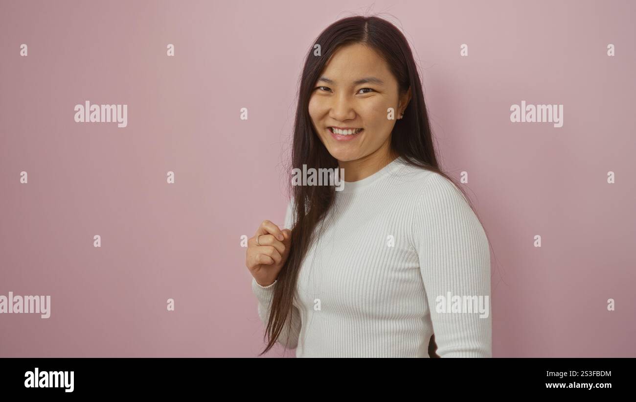 Frau lächelt isoliert vor einem rosafarbenen Hintergrund und zeigt Jugendlichen Stil und fröhliches Verhalten mit Betonung auf Schönheit und Eleganz. Stockfoto