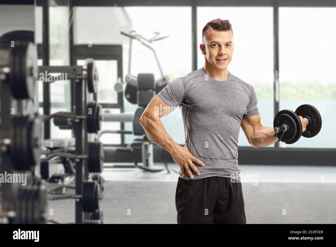 Junger Mann, der mit einer Hantel trainiert und in einem Fitnessstudio posiert Stockfoto