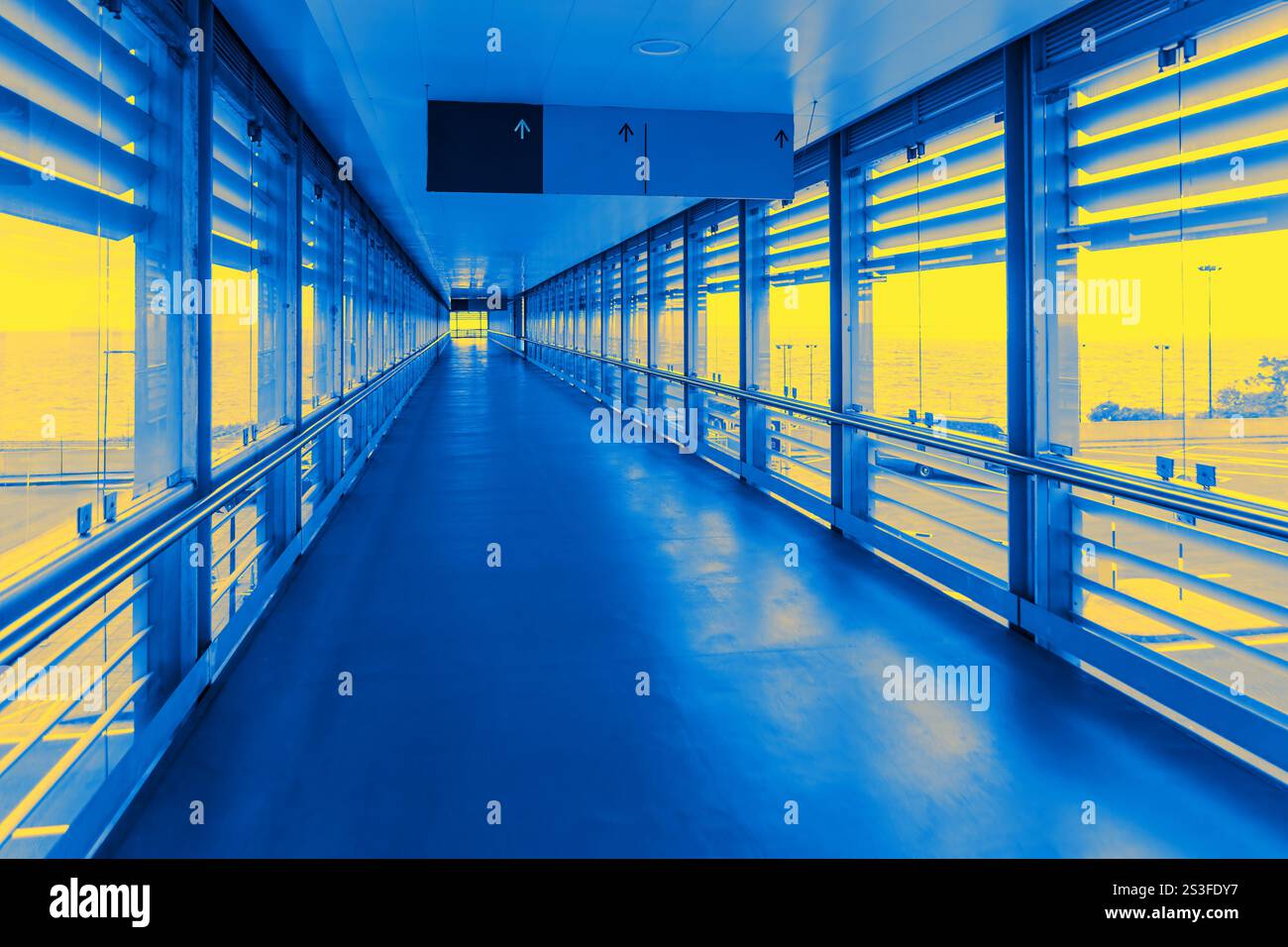 Moderner Flughafengang mit großen Glasfenstern und Metallgeländern, in markanter blau-gelber Beleuchtung getaucht, schafft einen futuristischen und lebendigen geldautomaten Stockfoto