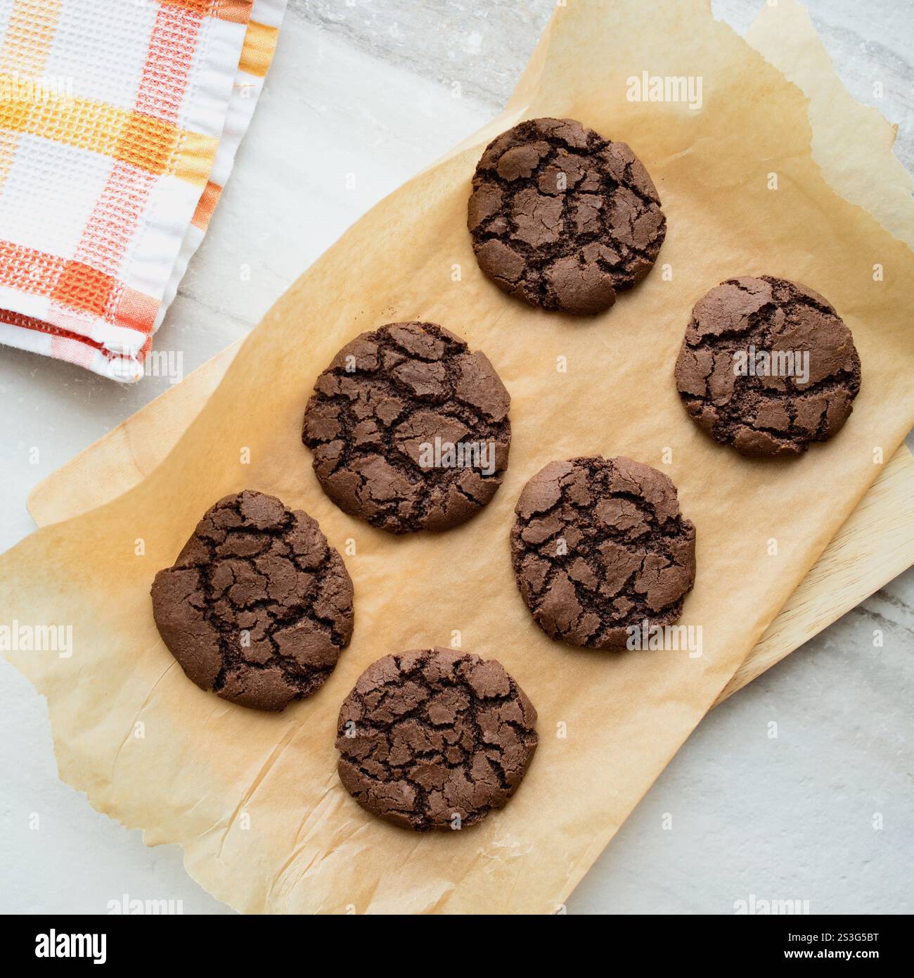 Frisch gebackene Schokoladen-Crinkle-Plätzchen werden in einer hellen Marmorküche mit orangefarbenen und weißen Akzenten präsentiert. Stockfoto