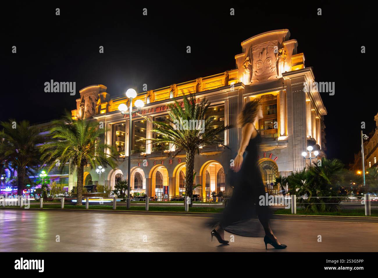 Eine Frau in einem schwarzen Kleid ist bewegungsunscharf, während sie entlang der beleuchteten Promenade des Anglais an der französischen Riviera in Nizza, Frankreich, spaziert Stockfoto