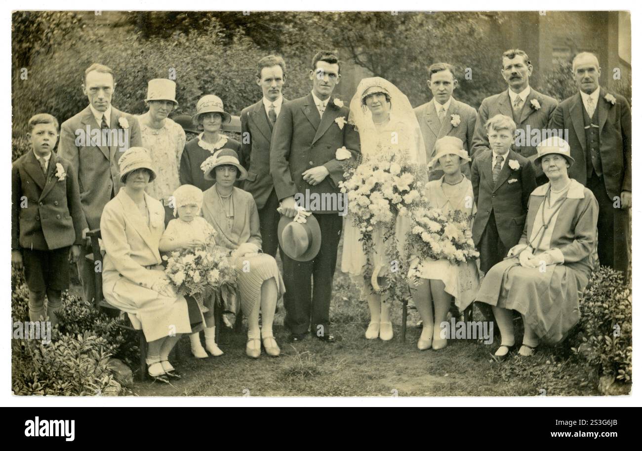Die Frauen tragen modische Cloche-Hüte, Brautbekleidung, Braut und Bräutigam und Brautjungfern, historische Kostüme, junge und ältere Leute, die für ein Hochzeitsfoto im Freien posieren, wunderschöne Sträuße und Posen, Blumen 1920. GROSSBRITANNIEN Stockfoto