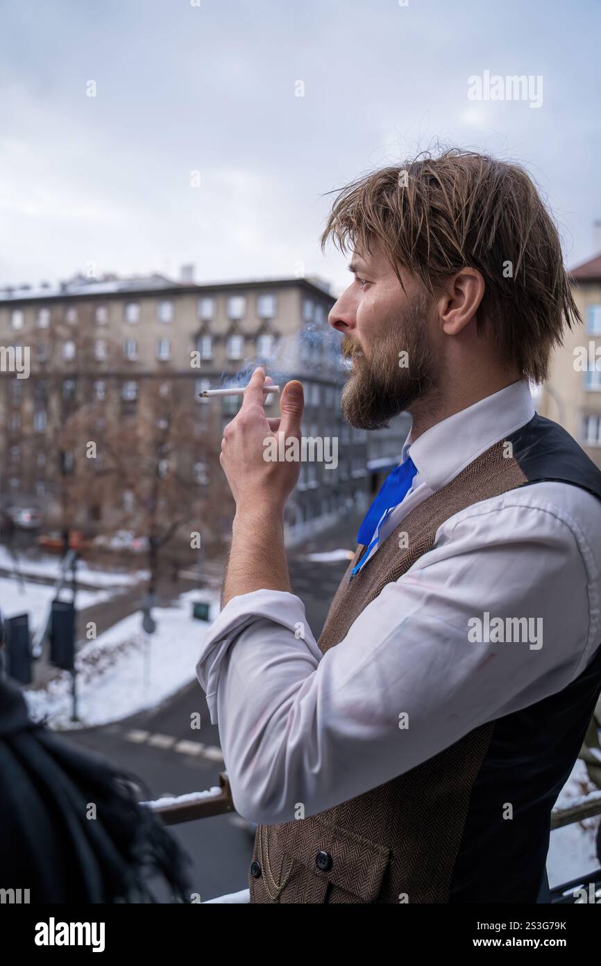 Ein nachdenklicher Mann in Vintage-Kleidung raucht auf einem Balkon und blickt auf eine ruhige urbane Szene unter weichem Tageslicht und strahlt eine nostalgische und introspektive Stimmung aus Stockfoto