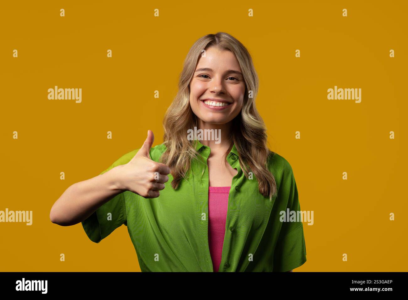 Stilvolle Frau mit Handzeichen, Daumen-hoch-Geste. Glückliche Dame, richtige perfekte Wahl, tolles Angebot, gelber Hintergrund. Positives weibliches Model lächelt Stockfoto