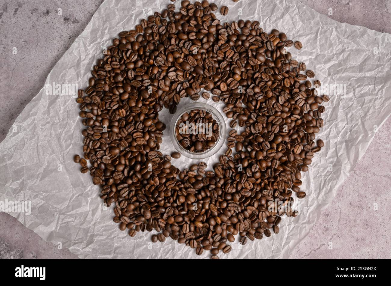Blick von oben auf frische aromatische Kaffeebohnen in einem kleinen Glas, umgeben von Kaffeebohnen auf hellem Hintergrund. Arabica- und Robusta-Mischung Stockfoto