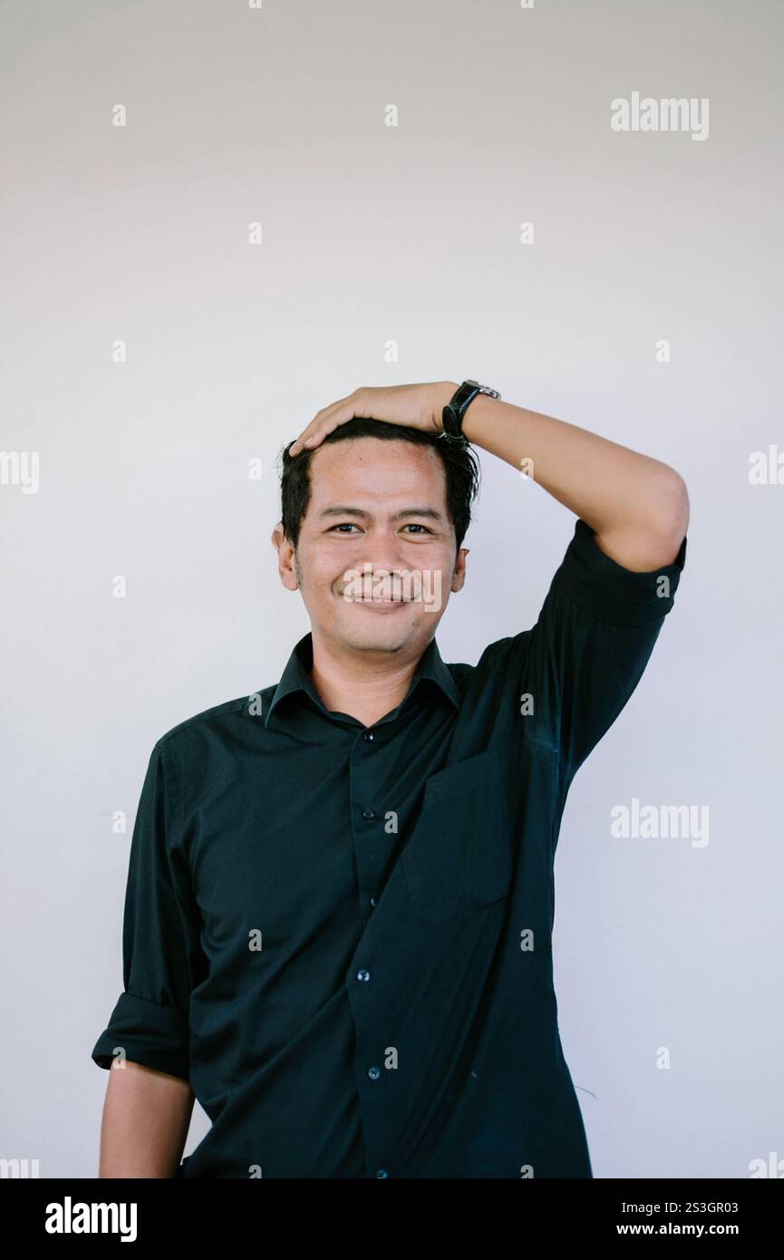 Ein fröhlicher junger Mann in einem schwarzen Hemd lacht fröhlich vor weißem Hintergrund und fängt einen ehrlichen und unbeschwerten Moment ein. Stockfoto