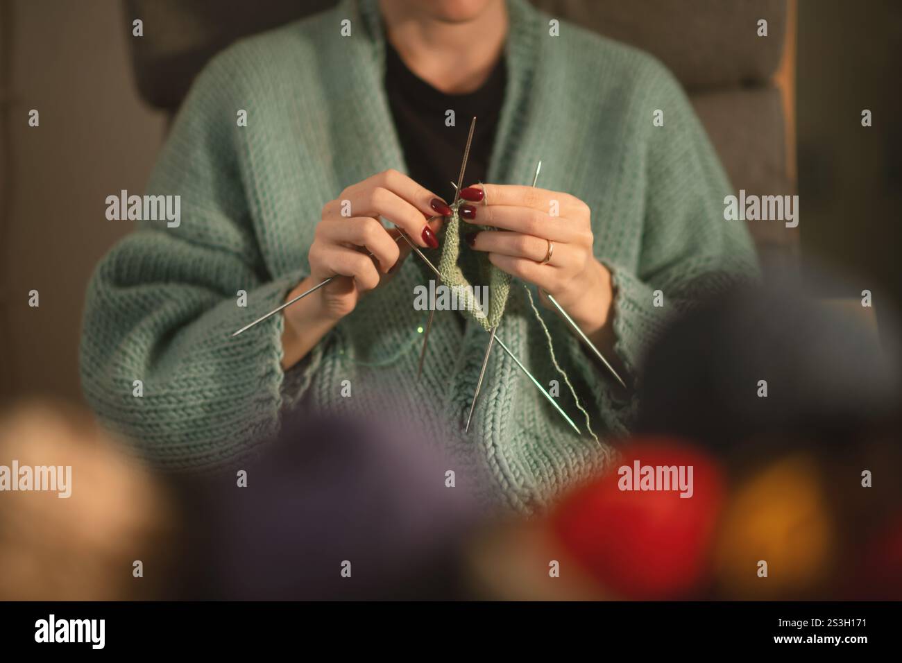 Eine detaillierte Ansicht der Hände einer jungen Frau, die sorgfältig mit grünem Garn gestrickt und mehrere Nadeln verwendet. Ein gemütlicher, fokussierter Moment der Kreativität Stockfoto