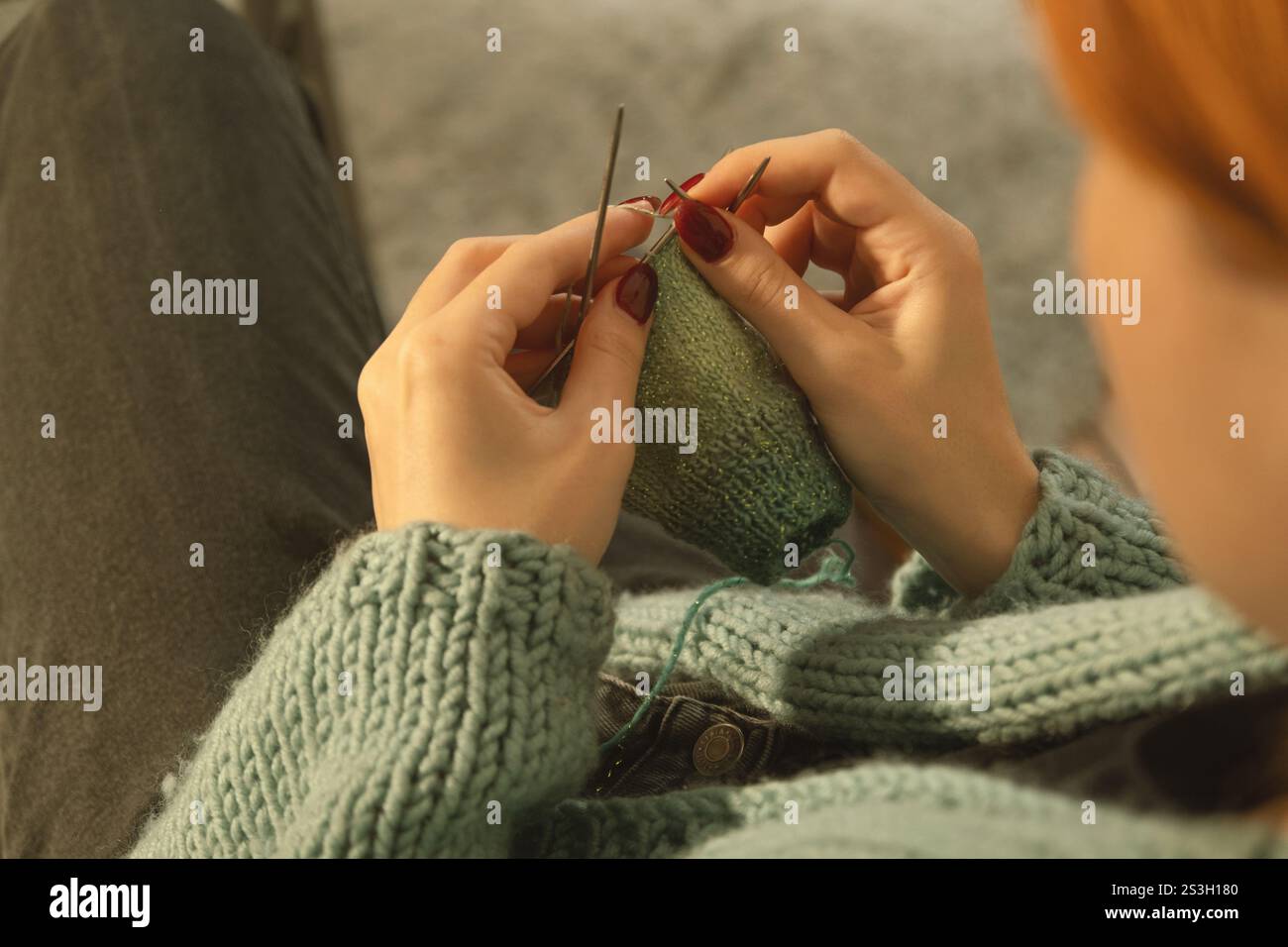 Eine detaillierte Ansicht der Hände einer jungen Frau, die sorgfältig mit grünem Garn gestrickt und mehrere Nadeln verwendet. Ein gemütlicher, fokussierter Moment der Kreativität Stockfoto