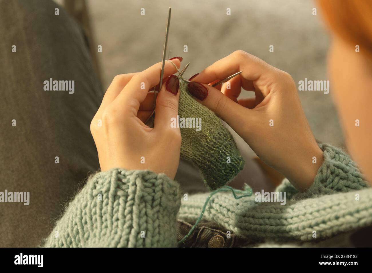 Eine detaillierte Ansicht der Hände einer jungen Frau, die sorgfältig mit grünem Garn gestrickt und mehrere Nadeln verwendet. Ein gemütlicher, fokussierter Moment der Kreativität Stockfoto