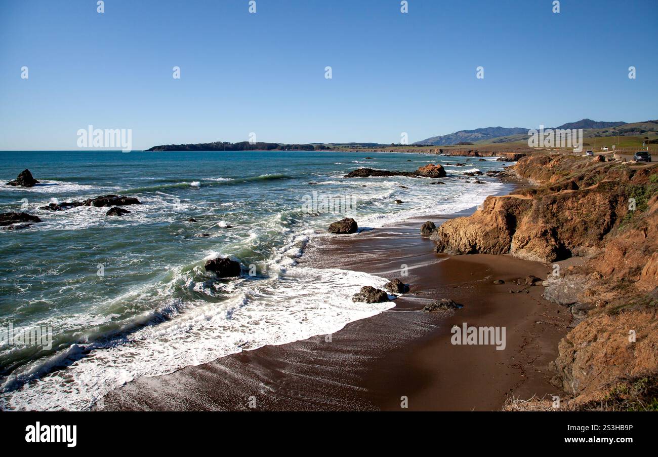 Eine ruhige Küstenlinie in Cambria, Kalifornien, erstreckt sich entlang der Küste, wo Wellen sanft auf Felsen am Pacific Coastal Highway prallen Stockfoto