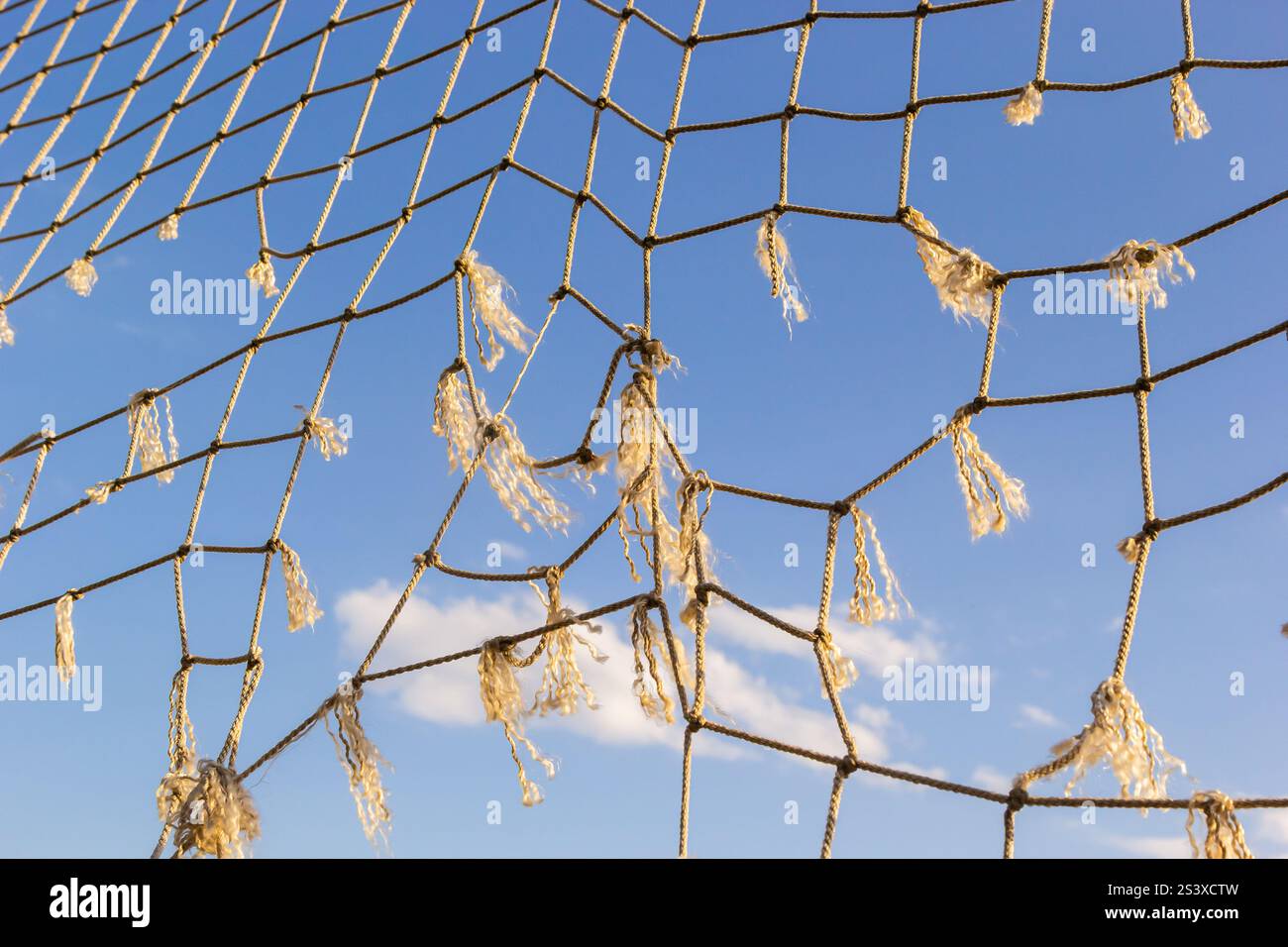 Das zerrissene Fischernetz zieht sich über den Rahmen und fängt das Sonnenlicht vor einem leuchtend blauen Himmel ein. Schlaue Wolken verleihen der ruhigen Kulisse dieses s Tiefe Stockfoto
