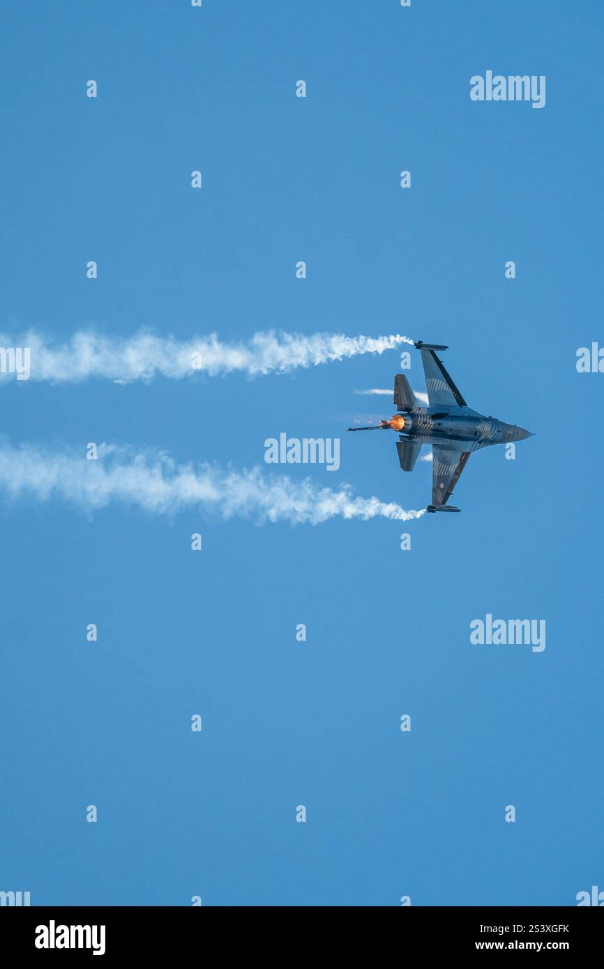 F-16-Kampfjet, der ein gewagtes Manöver am Himmel durchführt. Rauchspur. Stockfoto
