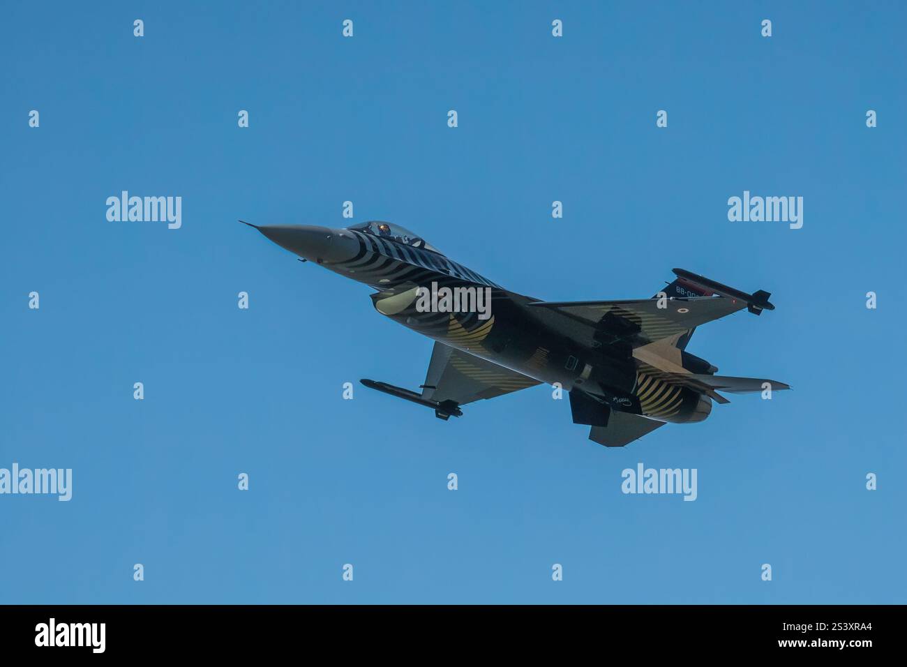 Der F-16-Kampfjet fliegt durch einen klaren blauen Himmel. Die charakteristische Tarnfarbe des Jets. Stockfoto