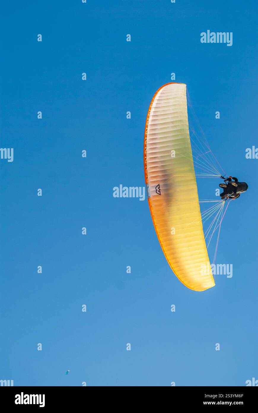 Leuchtender orangefarbener Gleitschirmflieger, der durch einen klaren blauen Himmel schwebt. Stockfoto