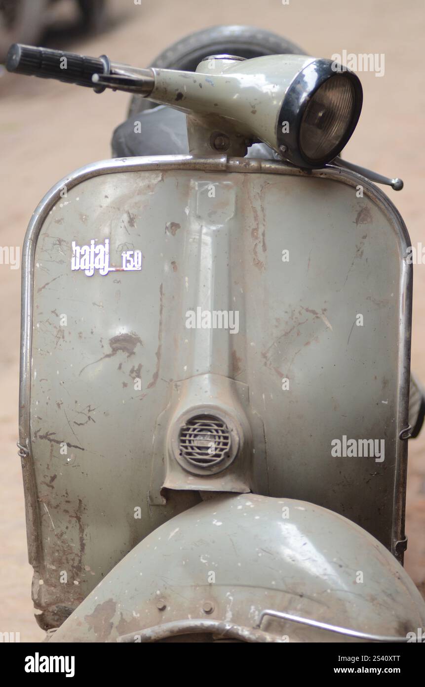 Klassischer Vintage-Roller parkt auf einer staubigen Straße in einem Stadtgebiet unter warmer Sonne am Nachmittag. Stockfoto