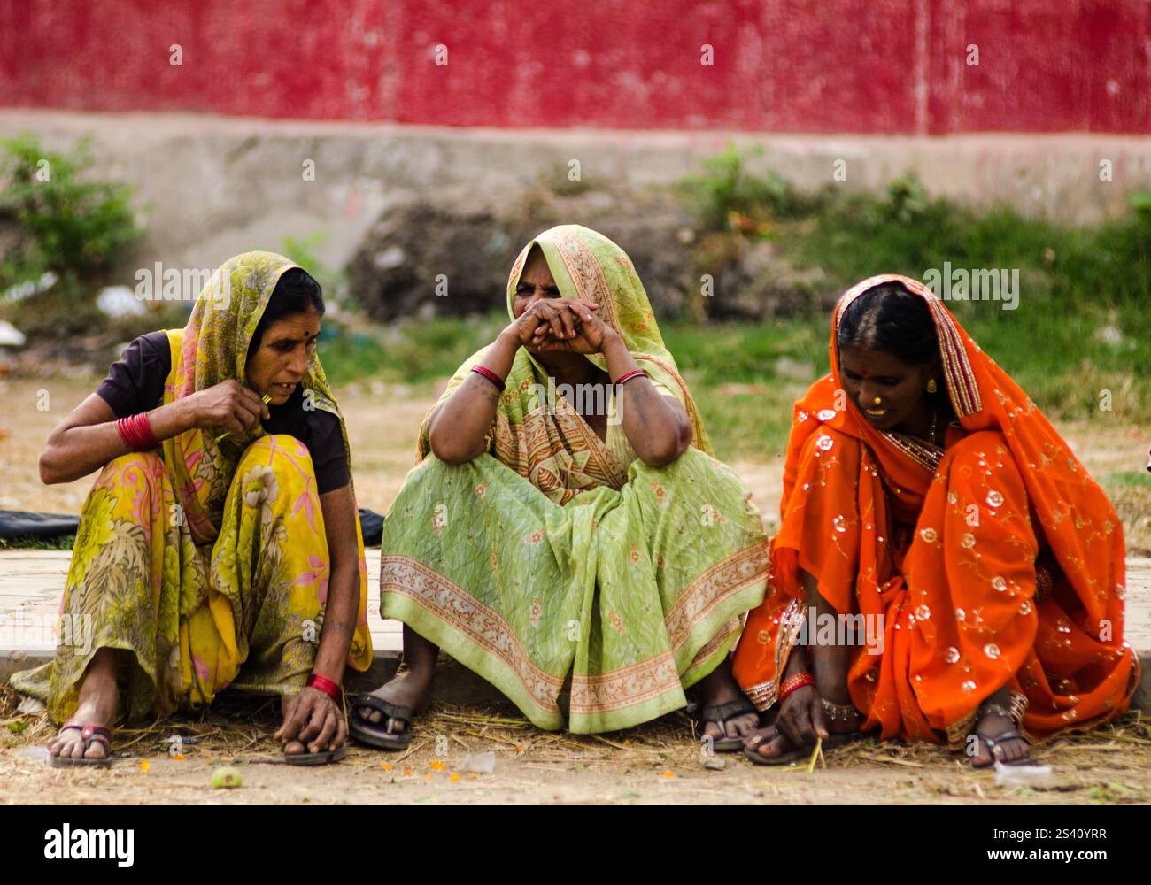 Drei Frauen in lebendiger traditioneller Kleidung sitzen eng zusammen auf dem Boden. Sie führen Gespräche und genießen die warme Atmosphäre. Stockfoto