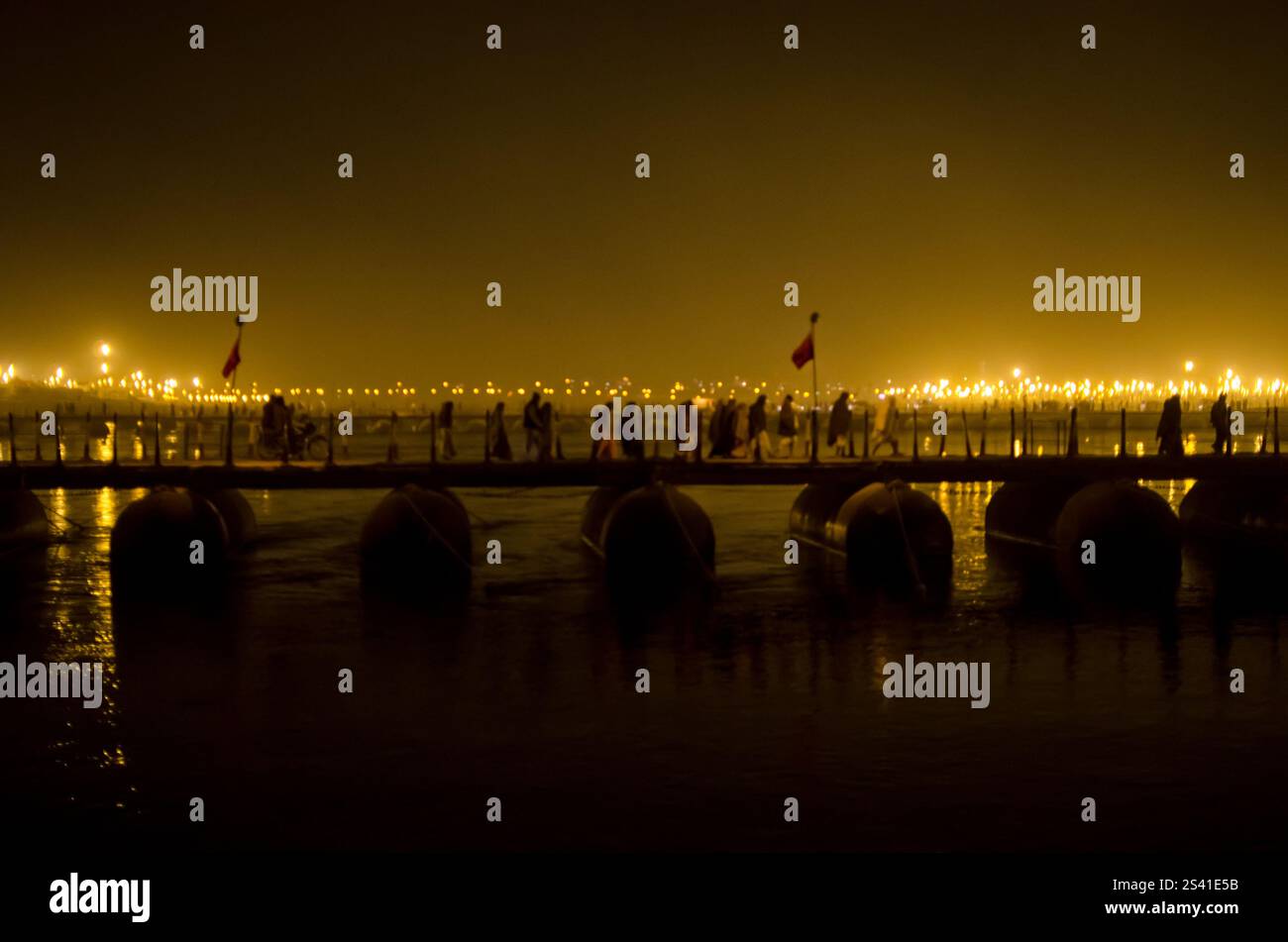 Leute, die nachts über eine Brücke laufen, unter warmen Lichtern am Fluss Stockfoto
