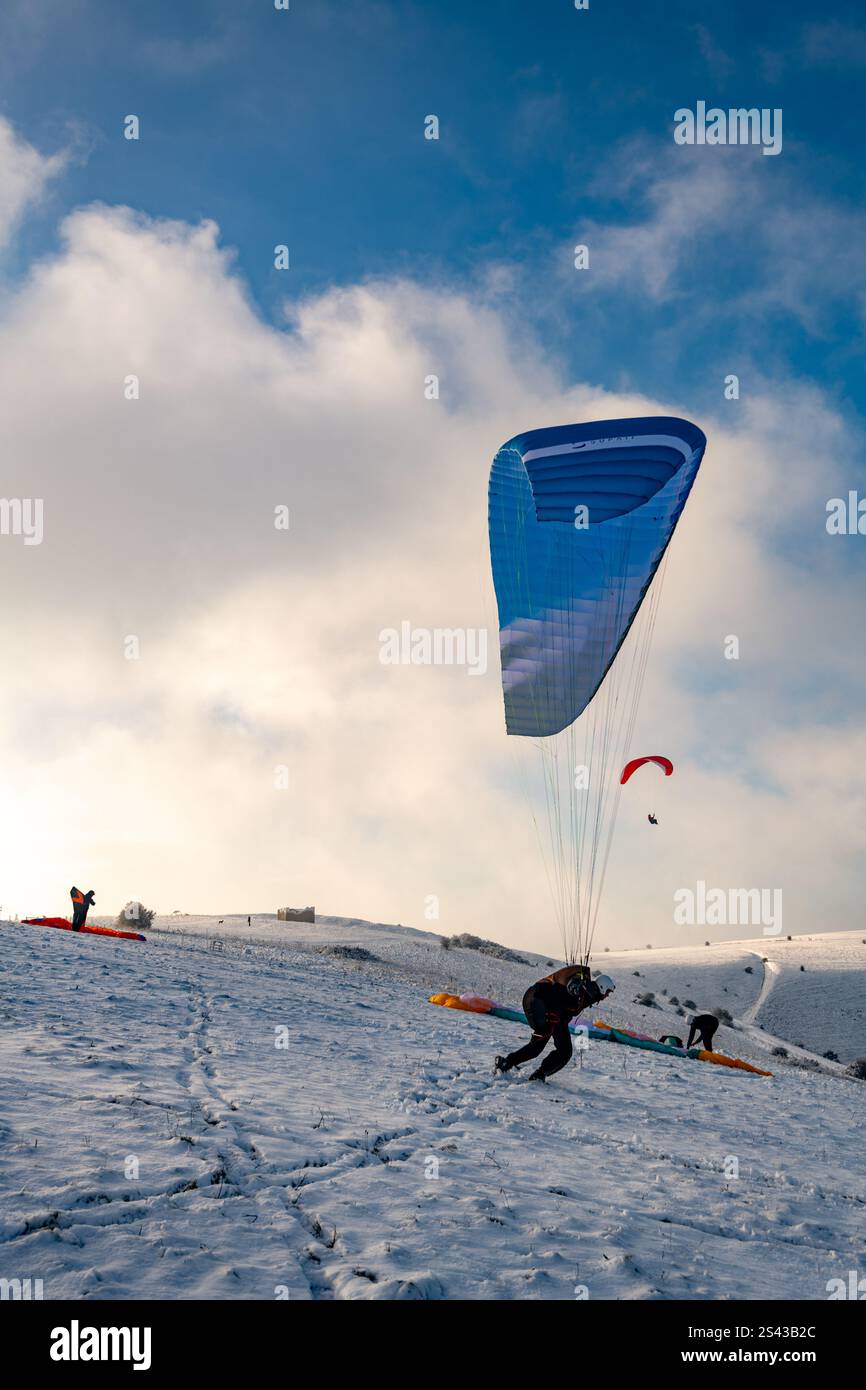 Paraglider fliegen nach einem unerwarteten starken Schneefall über die South Downs am Devil's Dyke West Sussex über schneebedeckte Hügel Stockfoto