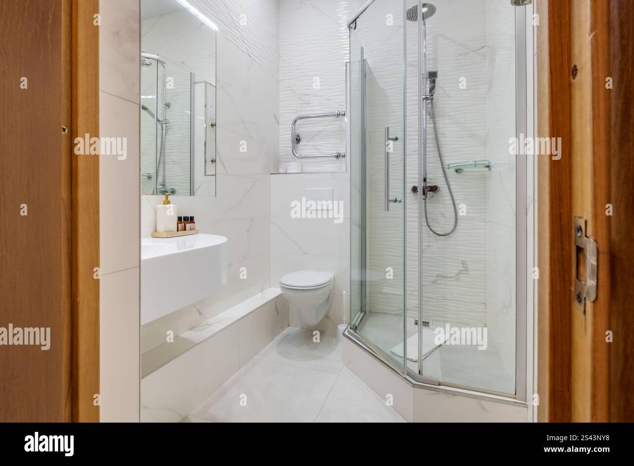 Ein sauberes und modernes Bad mit Glasdusche, wandmontierter Toilette, Handtuchwärmer und Fliesen im Marmorstil. Stockfoto