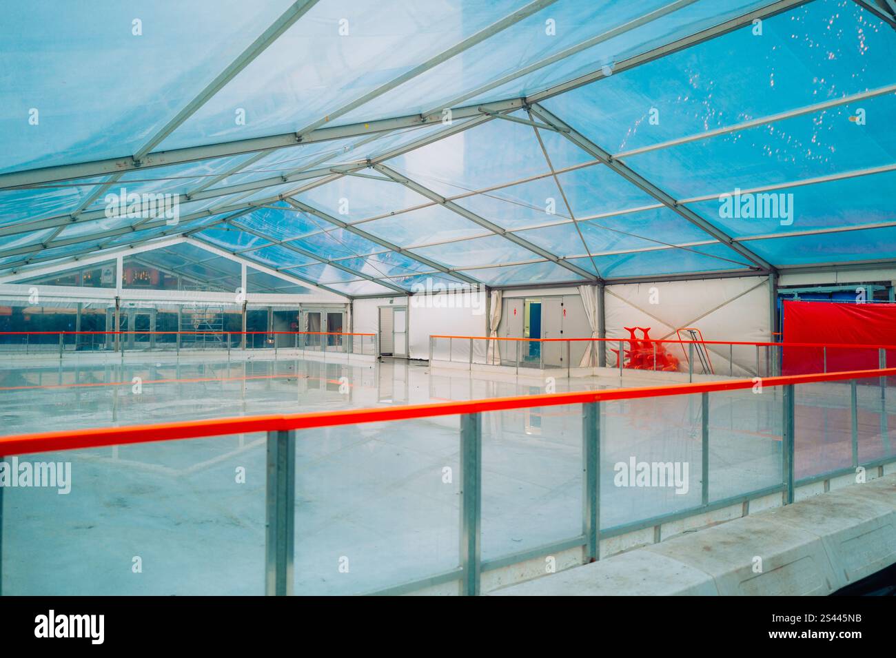 Eislaufbahn mit klarem blauem Dach, hellroten Sicherheitsgeländern und Eislaufhilfen bietet eine moderne und unterhaltsame Atmosphäre. Stockfoto