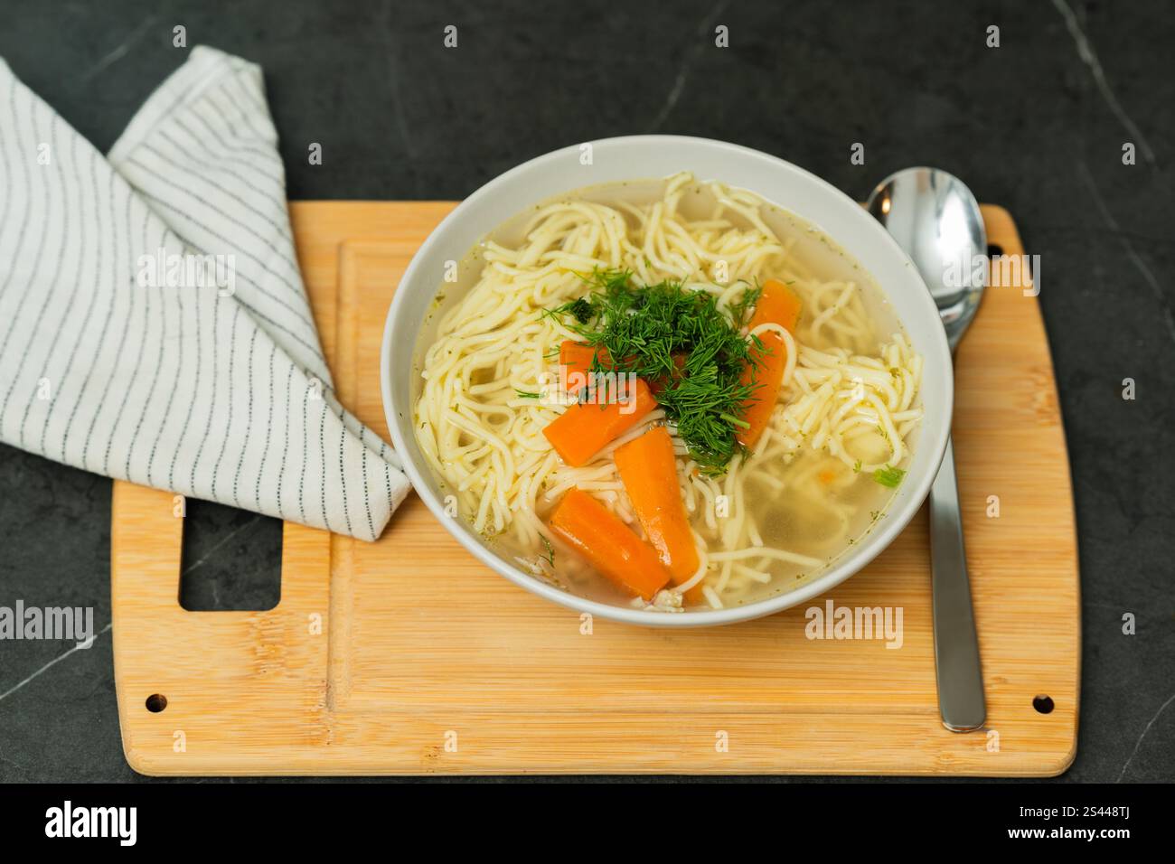 Aus nächster Nähe sehen Sie eine Schüssel mit hausgemachter Hühnchennudelsuppe, garniert mit frischem Dill und lebhaften Karottenscheiben. Das Gericht ist Stockfoto