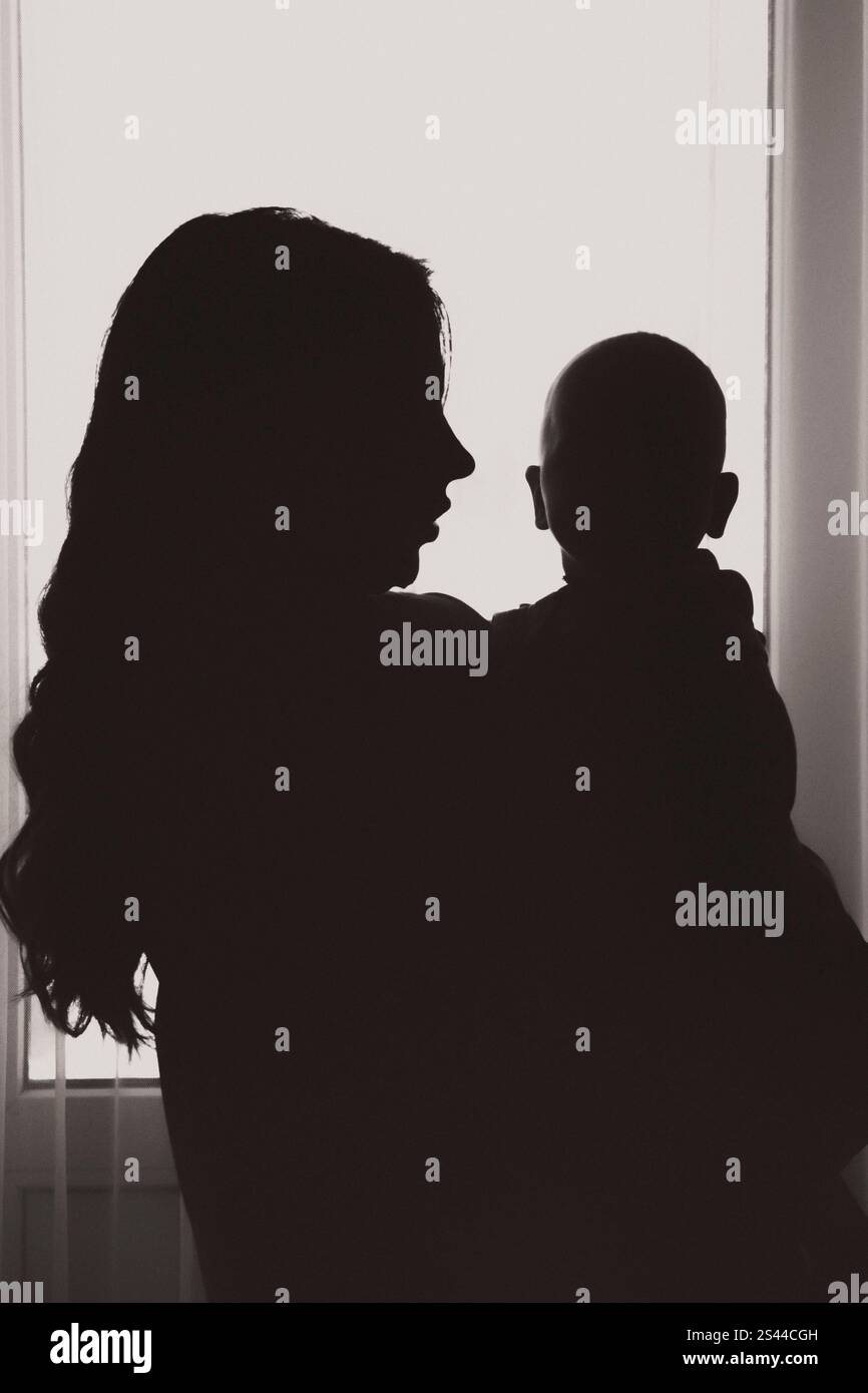 Silhouette einer Mutter, die ihr Kind sanft hält, eine herzerwärmende und intime Darstellung von Liebe, Fürsorge und der Bindung zwischen Eltern und Kind. Stockfoto