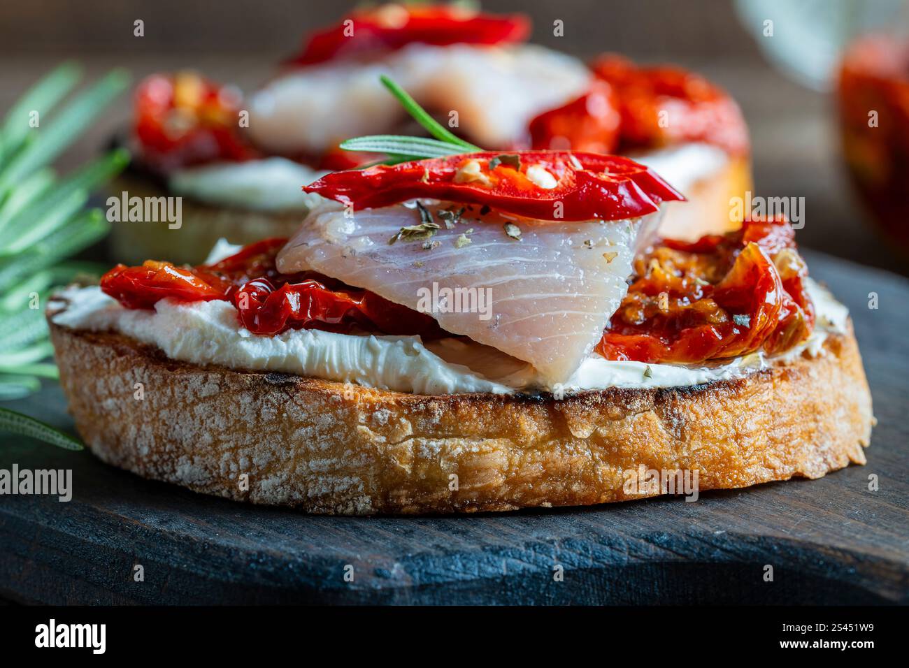 Zwei Brotscheiben mit Ricotta, Heringsstücken und sonnengetrockneten roten Tomaten auf Holzbrett Hintergrund. Köstliches Frühstück oder Wein-Snack. Clos Stockfoto