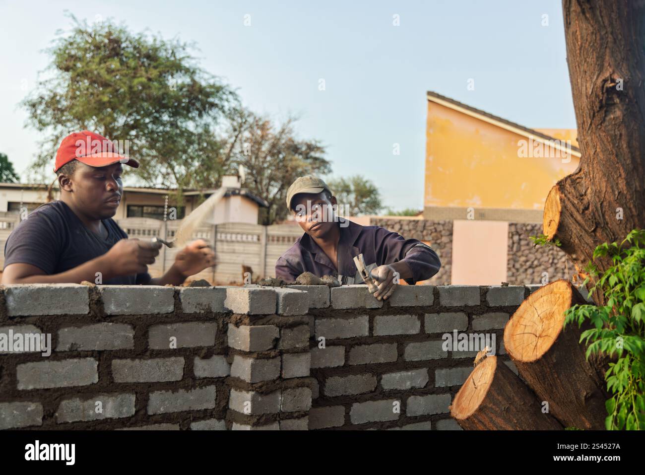 Maurer afrikanische Männer Kollegen, mit einer Kelle und einem Hammer, bauen eine Mauer bei Sonnenuntergang draußen Stockfoto