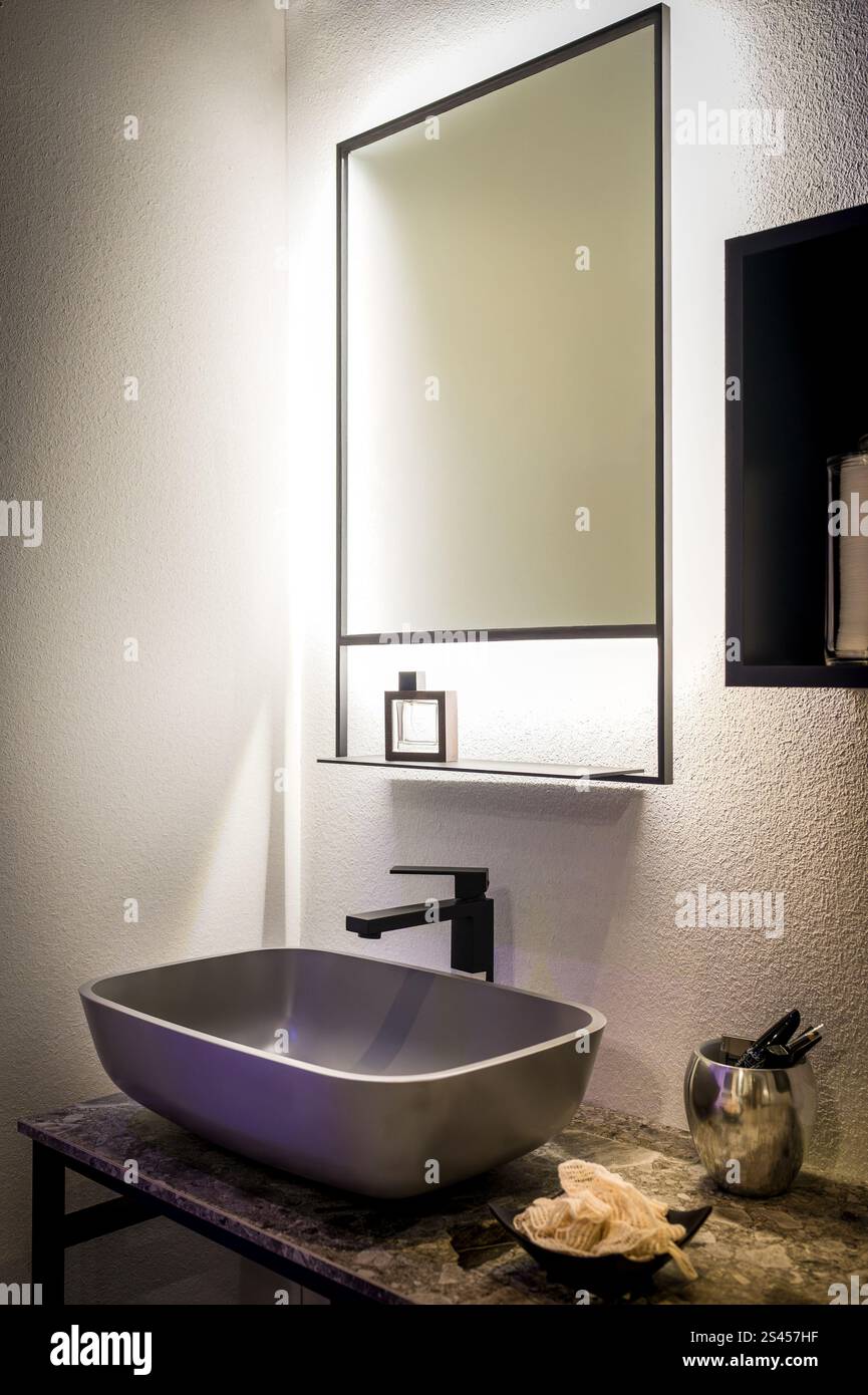 Das moderne Badezimmer verfügt über einen beleuchteten Spiegel, ein stilvolles Waschbecken und moderne Designelemente Stockfoto