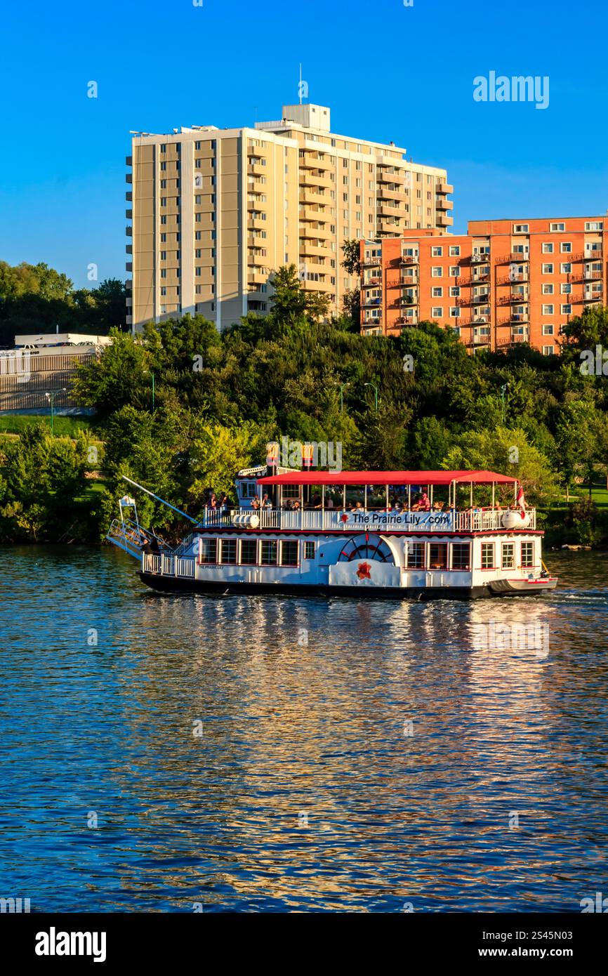Ein Boot mit einem rot-weiß gestreiften Oberteil schwimmt auf einem Fluss. Das Boot fährt auf ein großes Gebäude zu Stockfoto
