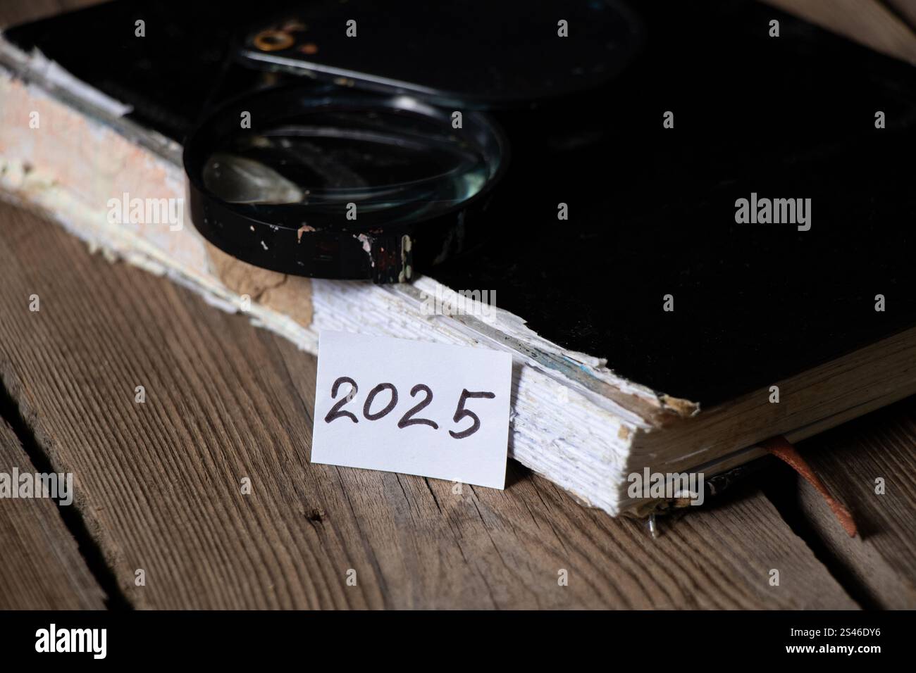 Ein altes zerrissenes Notizbuch, eine Lupe und eine Karte mit dem Text 2025 liegen auf einem Holztisch, das Jahr 2025 Stockfoto