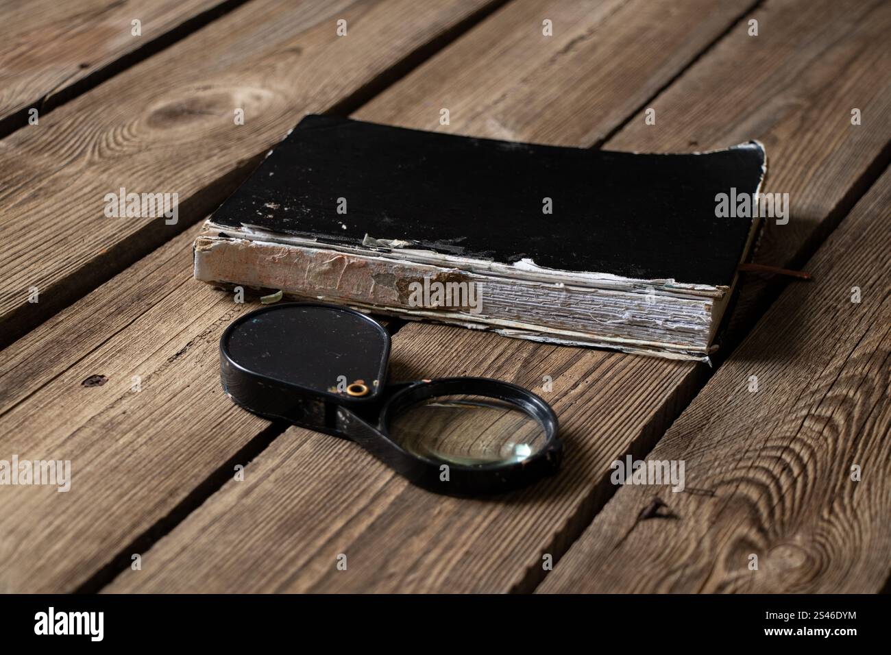Ein altes zerrissenes Notizbuch und eine Lupe liegen auf einem Holztisch, ein Tagebuch Stockfoto