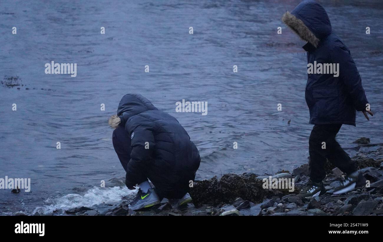 Kinder erkunden an einem kalten Wintertag die felsige Küste, gekleidet in warmen Jacken, und genießen Outdoor-Abenteuer am ruhigen Wasser. Stockfoto