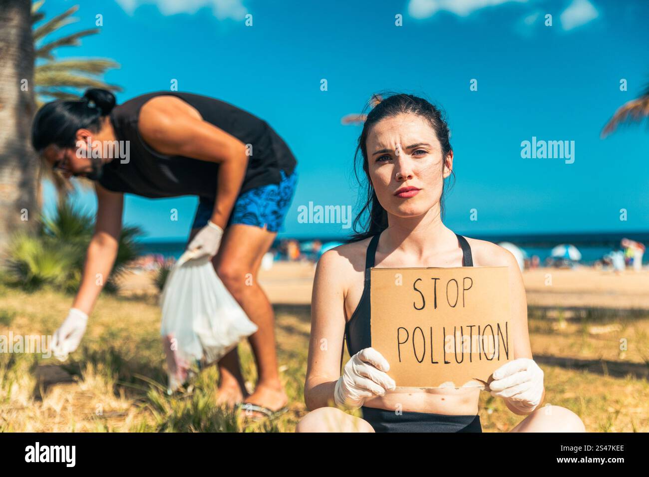 Eine Aktivistin hält ein Schild, auf dem steht: „Stoppt die Verschmutzung am Strand. Ihr Kollege sammelt Müll. Stockfoto