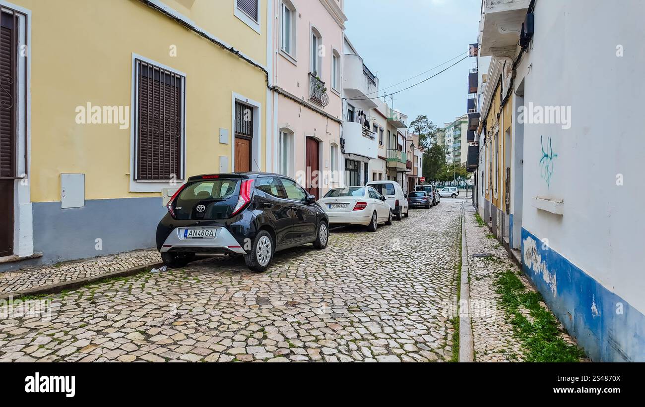 Eine enge Straße in Portimão, Portugal, gesäumt von Gebäuden und mit Autos, die entlang der Seite geparkt sind. Stockfoto