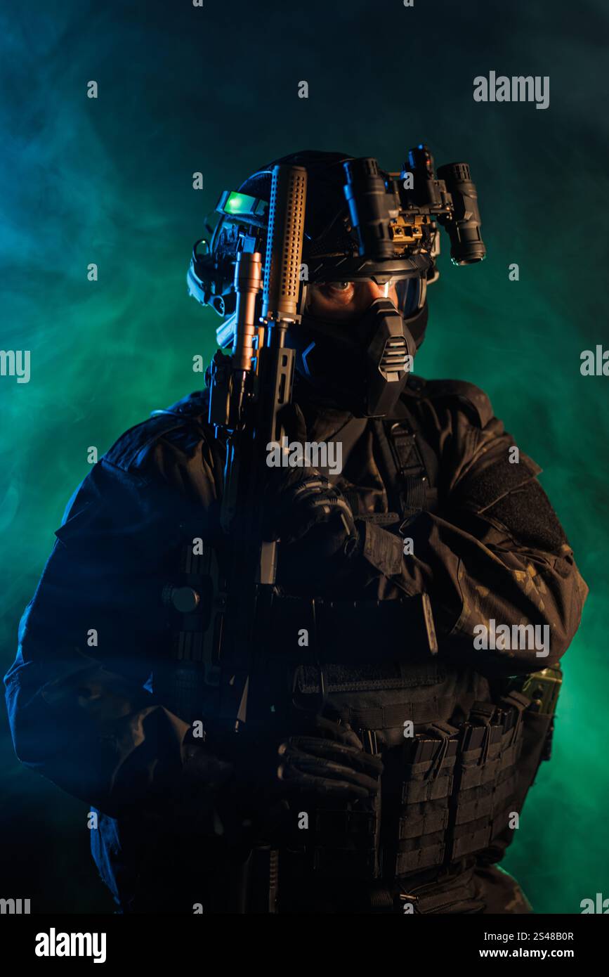Ein taktischer Soldat in voller Kampfausrüstung und Nachtsichtbrille, der stoisch in einer grün gefärbten rauchgefüllten Atmosphäre posiert. Die Bildkontraktion Stockfoto