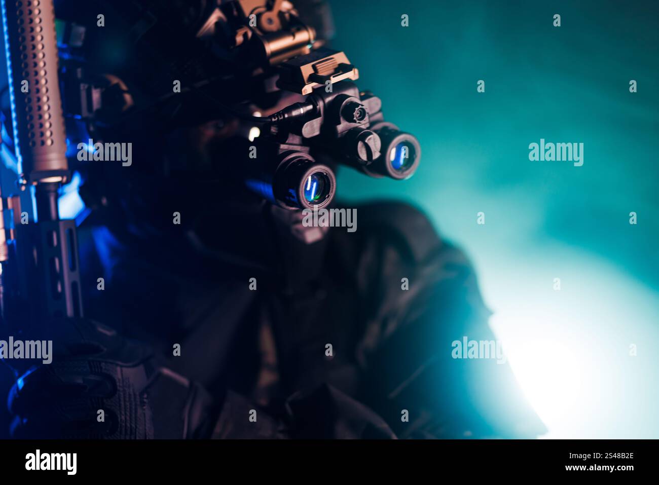 Ein Spezialeinsatzmann in taktischer Ausrüstung hält eine Waffe und benutzt eine Nachtsichtbrille in einem dramatischen Grün- und Blaulicht-Setup für ein c Stockfoto