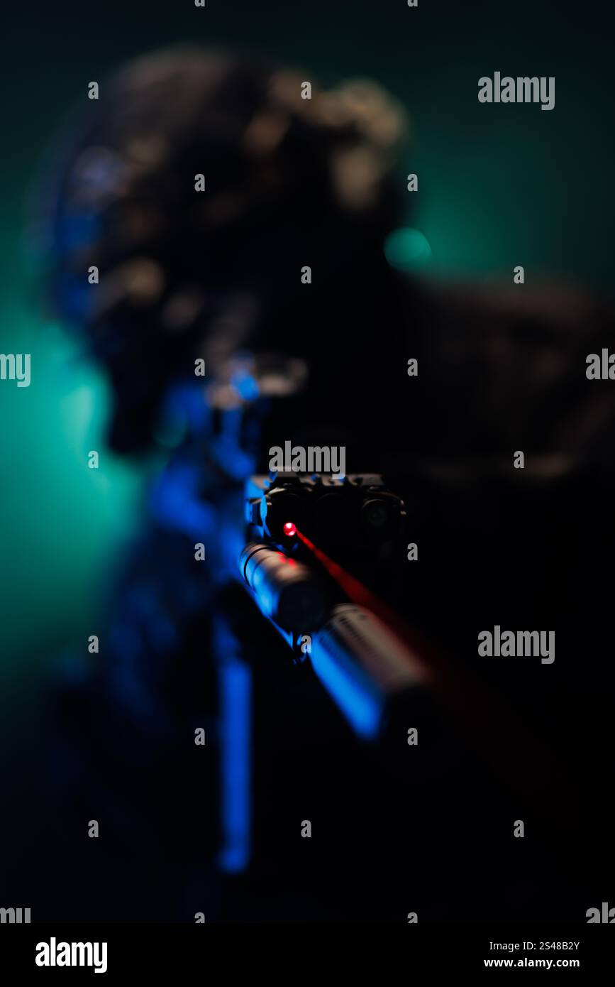 Ein taktischer Profi konzentriert sich auf ein langes Gewehr mit rotem Laservisier in einer dramatischen Szene bei schlechten Lichtverhältnissen, die Präzision, Tarnung und Kampfbereitschaft suggeriert Stockfoto