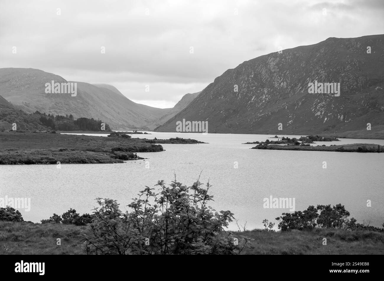 Das Bild ist ein Schwarzweißfoto eines Sees, der von Bergen umgeben ist. Das Wasser ist ruhig und ruhig und spiegelt die Berge in der Ferne wider. Die sce Stockfoto