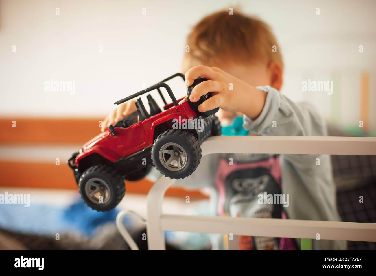 Ein kleines Kind konzentriert sich darauf, ein rotes Spielzeugauto über den Rand einer Bettschiene zu manövrieren und dabei Kreativität und Konzentration während des Spielens in HO zum Ausdruck zu bringen Stockfoto