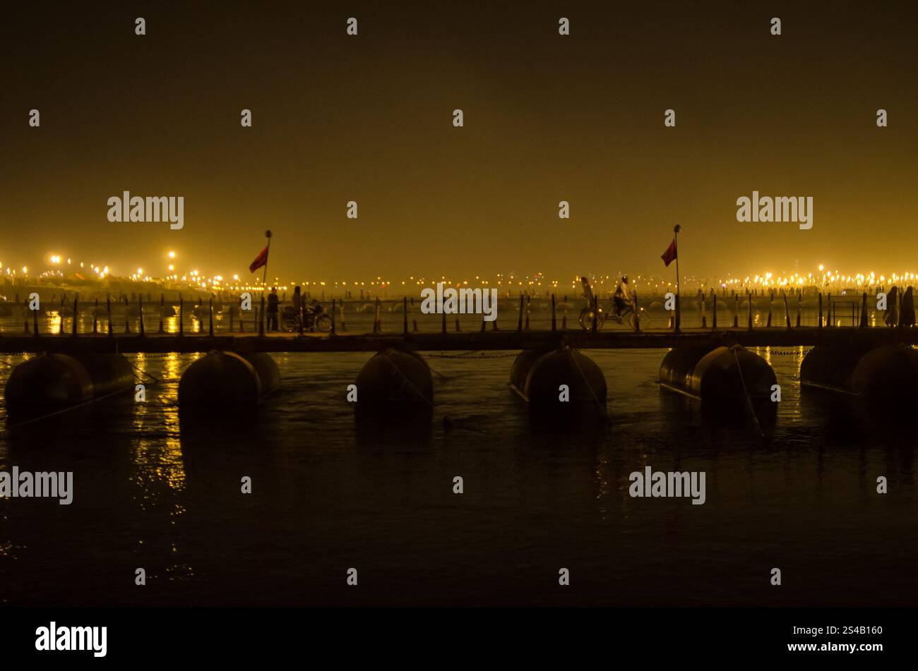 Leute, die nachts über eine Brücke laufen, unter warmen Lichtern am Fluss Stockfoto