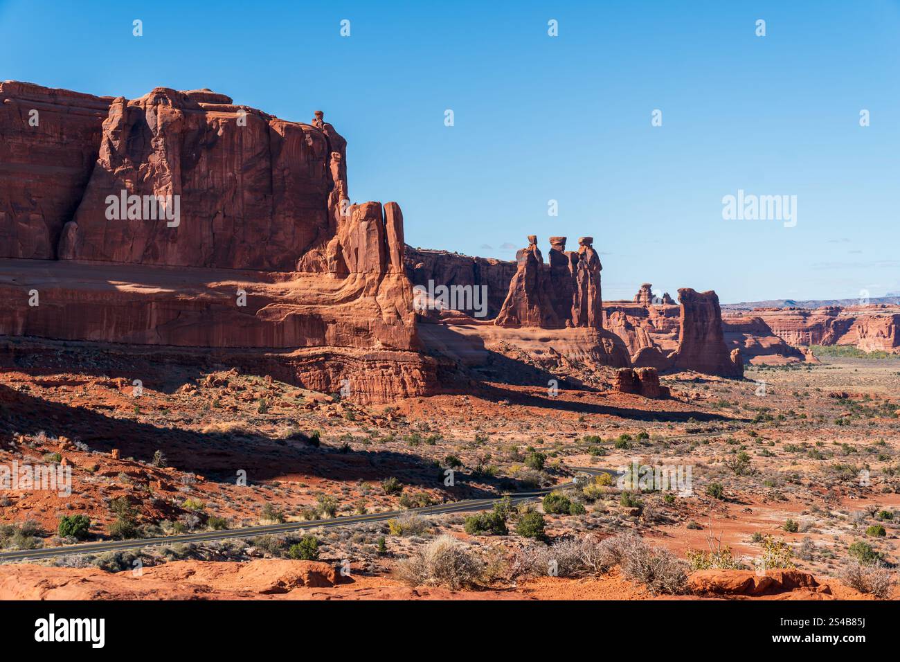 Die drei Klatschbasen und die rotsteinernen Formationen des Turms von Babel erheben sich über einer kurvenreichen Landschaftsstraße im Arches Nationalpark in der Nähe von Moab, Utah Stockfoto
