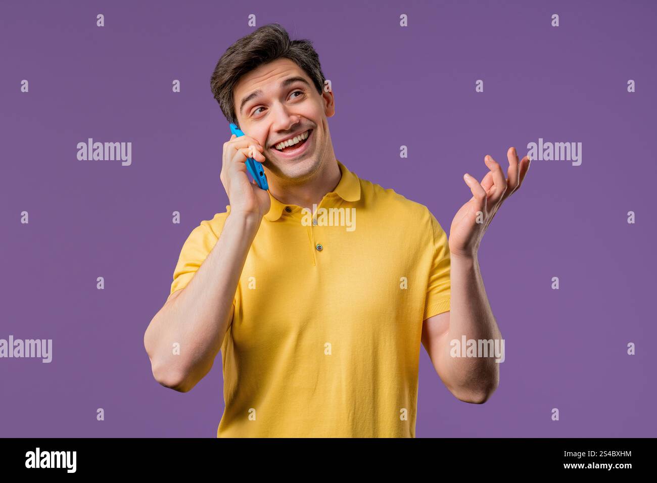 Lächelnder positiver Kerl, der telefoniert, netter Witz, lächelnd. Junger Mann auf violettem Hintergrund. Telefonieren mit dem Smartphone. Hohe Qualität Stockfoto
