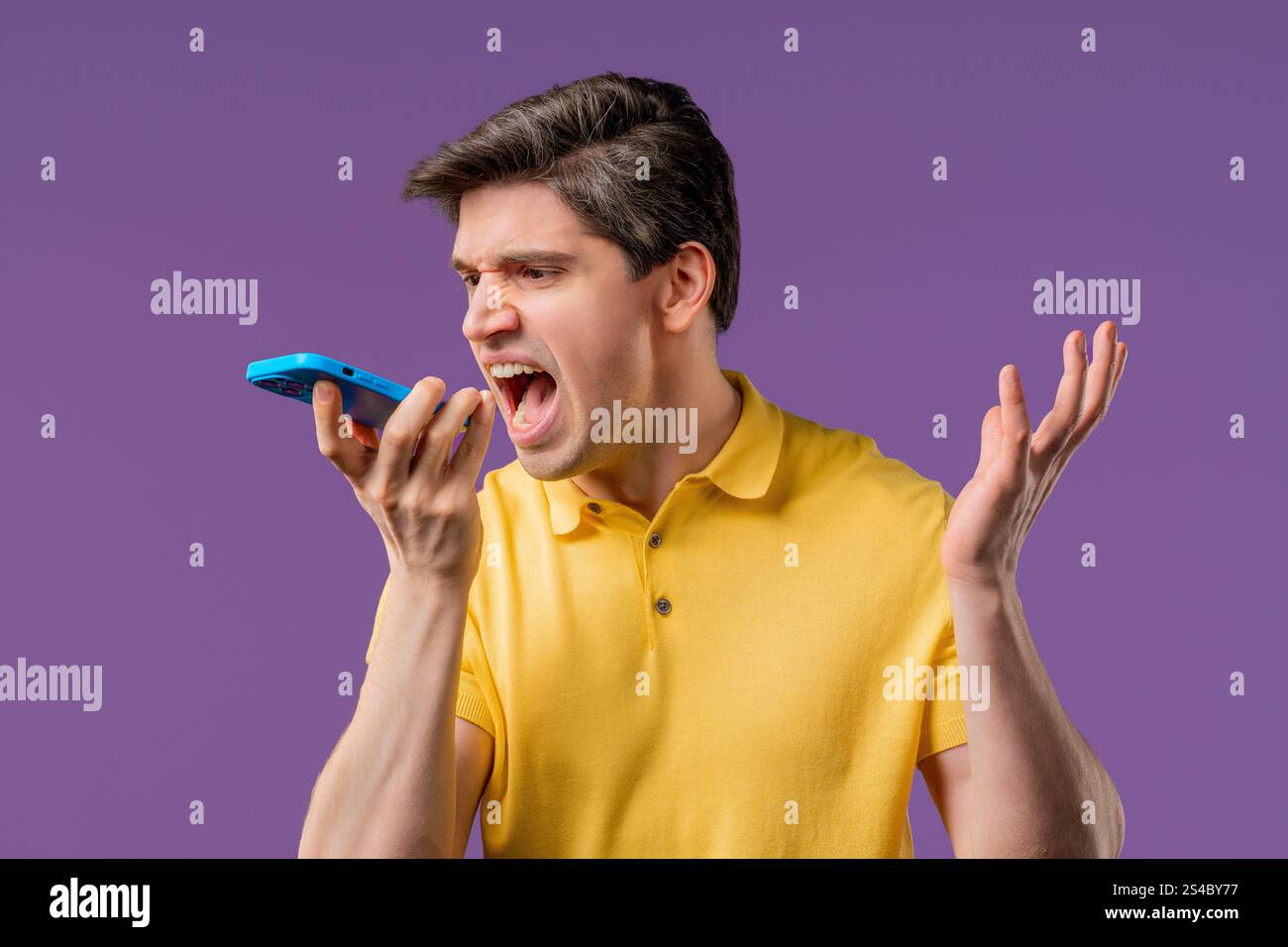 Verärgerter junger Mann, der sich streitet, während er auf dem Handy spricht. Wütender Kerl, Stress. Violetter Studiohintergrund. Konflikt, Streit, negativ. Hohe Qualität Stockfoto