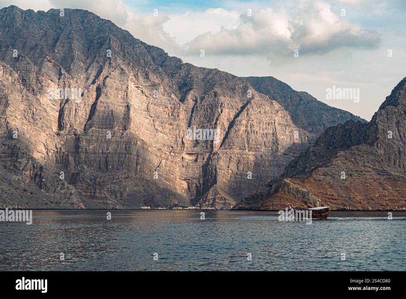 Eine traditionelle Dhow segelt durch die dramatischen Fjorde von Khasab, Oman und zeigt die raue Schönheit und das reiche maritime Erbe der Region. Stockfoto