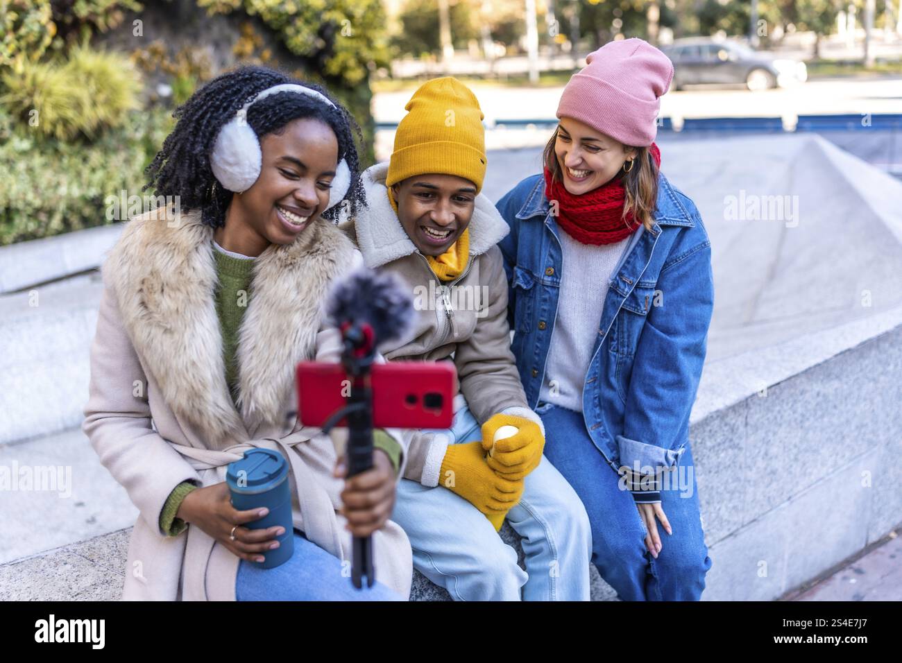 Eine Gruppe fröhlicher junger Content-Ersteller filmt einen Video-Blog im Freien in einer Winterstadt mit Smartphone und externem Mikrofon Stockfoto