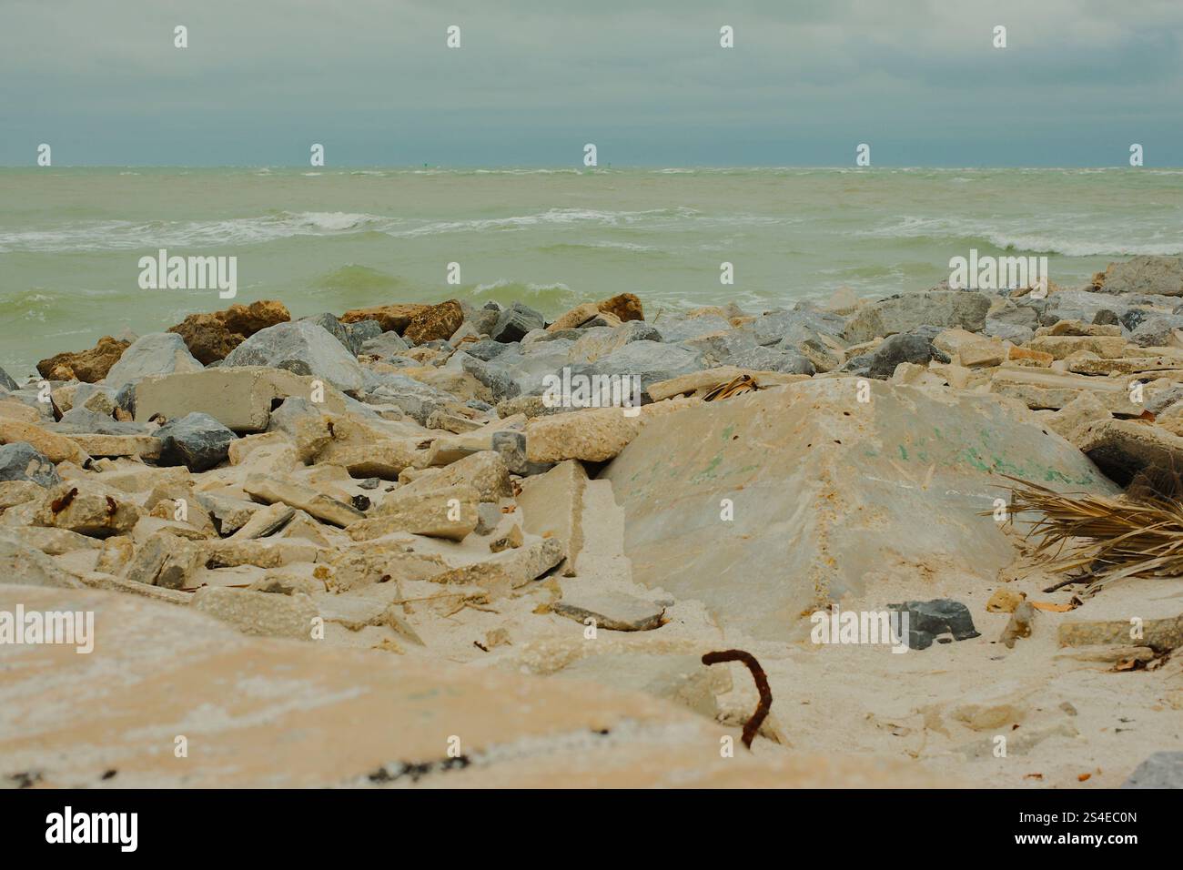 Niedrige Aussicht über große Felsen am St. Pete Beach, Florida, große weiße Wellen, die auf und über große Felsen plätschern. In Richtung Shell Key. Auf einem bewölkten d Stockfoto