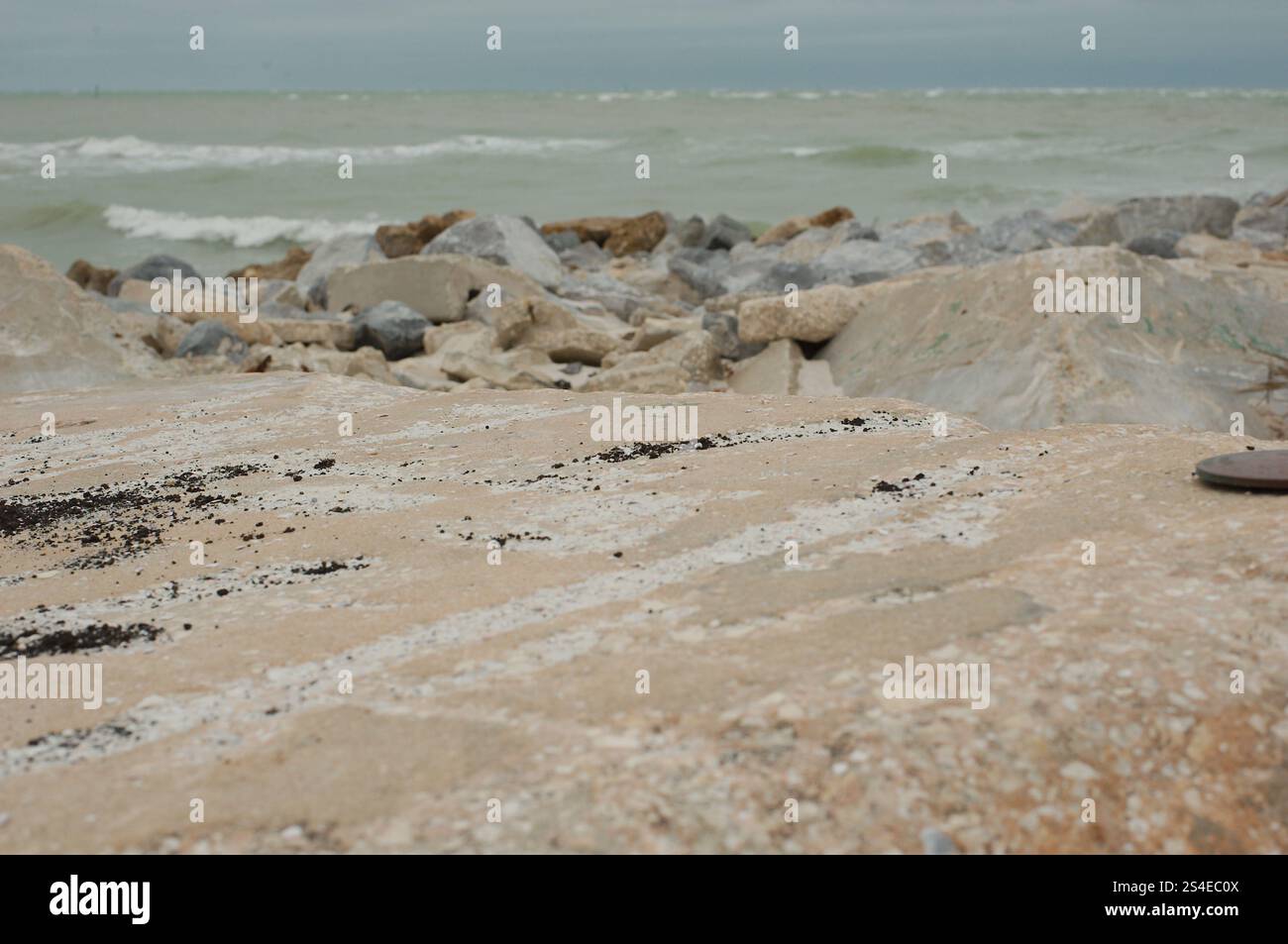 Niedrige Aussicht über große Felsen am St. Pete Beach, Florida, große weiße Wellen, die auf und über große Felsen plätschern. In Richtung Shell Key. Auf einem bewölkten d Stockfoto