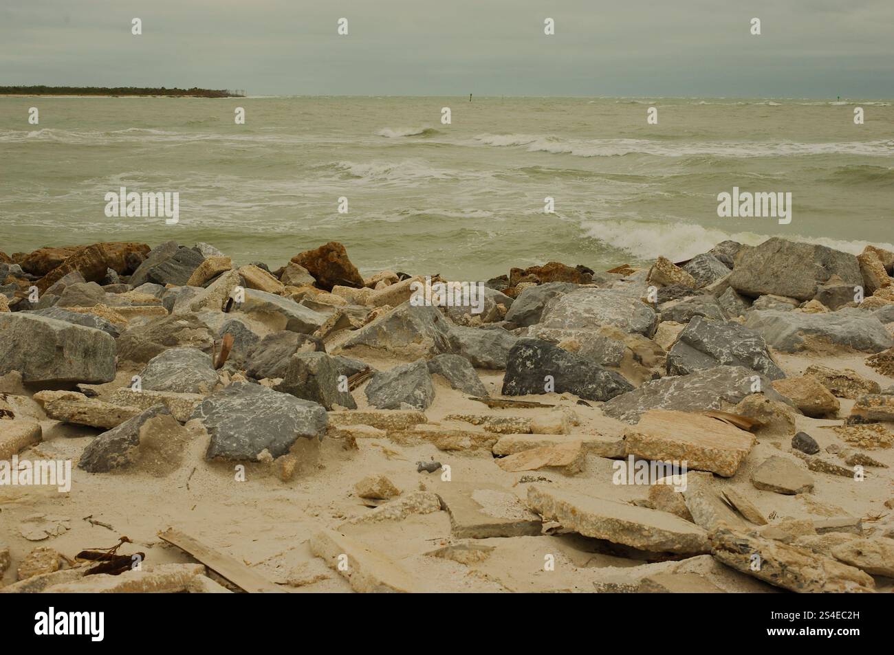 Niedrige Aussicht über große Felsen am St. Pete Beach, Florida, große weiße Wellen, die auf und über große Felsen plätschern. In Richtung Shell Key. Auf einem bewölkten d Stockfoto